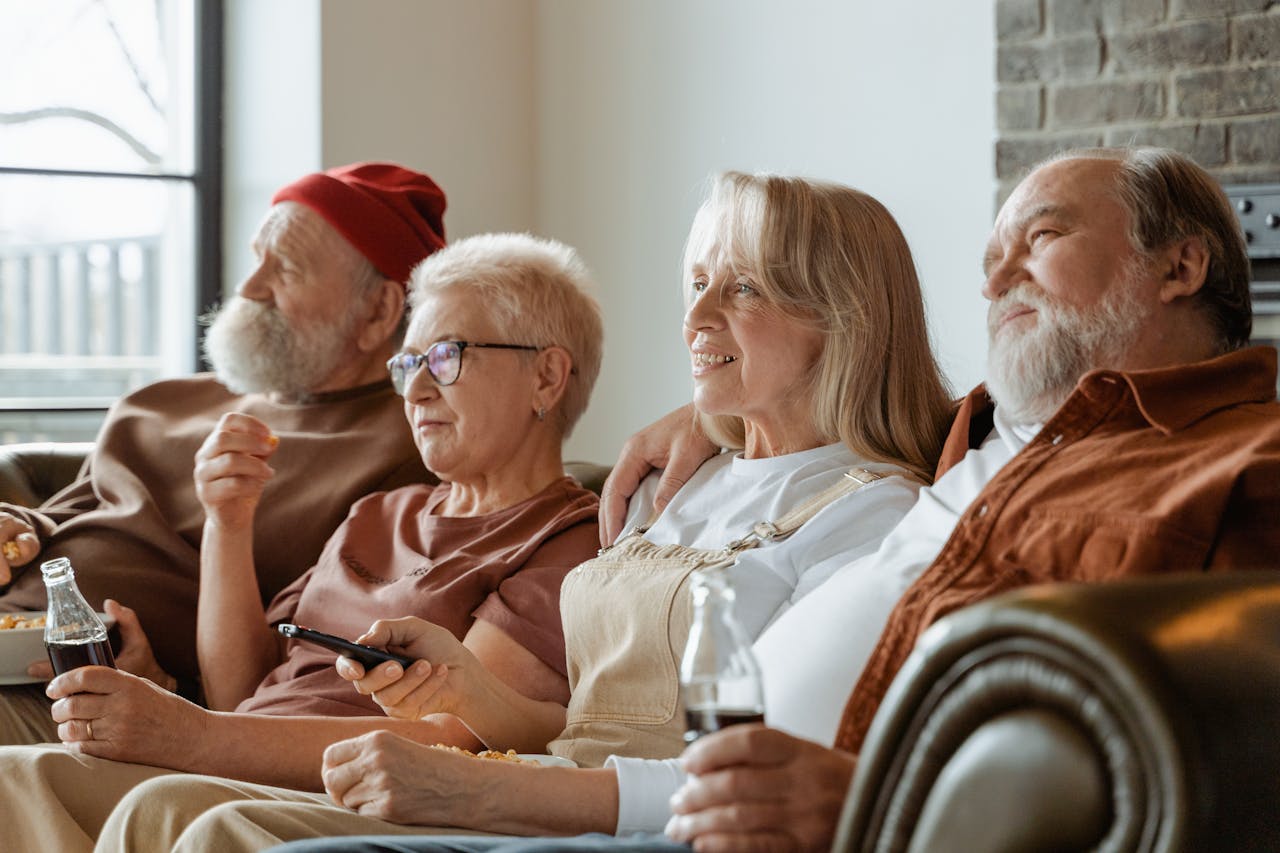 A group of senior adults sharing a cozy moment in a living room, enjoying snacks and drinks.